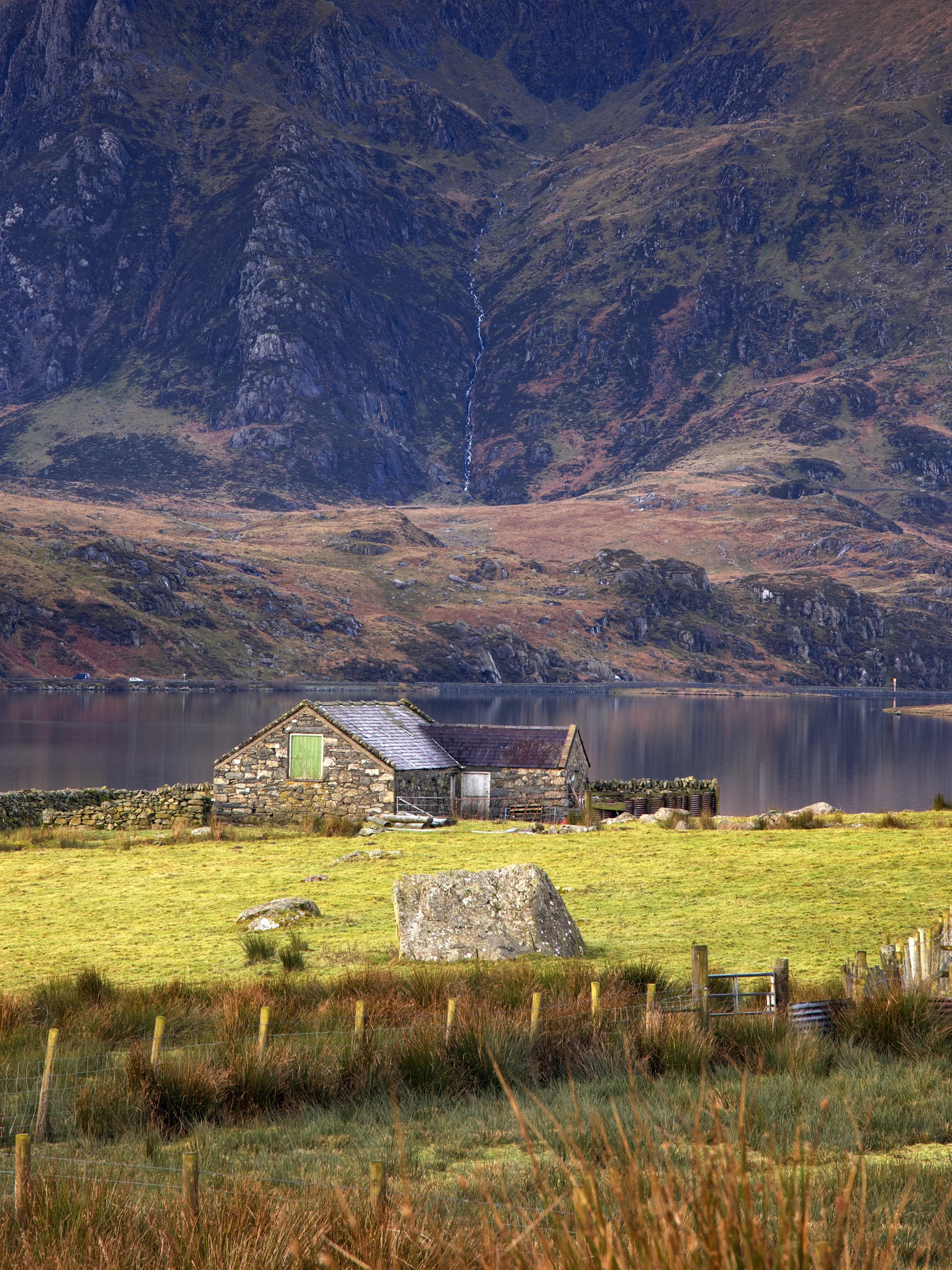 There's a strong chance this image contains the following subjects: house,  landscape,  lake,  travel,  nature,  farm,  grass,  wales,  snowdonia,  eryri,  eryrinationalpark,  nationalpark,  snowdon. The photographer has provided the following description: An old farmhouse on the edge of Llyn Ogwen in Snowdon. Photographer_name: Chris Michael. Title: Llyn Ogwen. The photographer has provided the following description: An old farmhouse on the edge of Llyn Ogwen in Snowdon. Make: canon. Model: EOS R. Technical: 70-200mm. Published: 2025-09-09 16:42:17