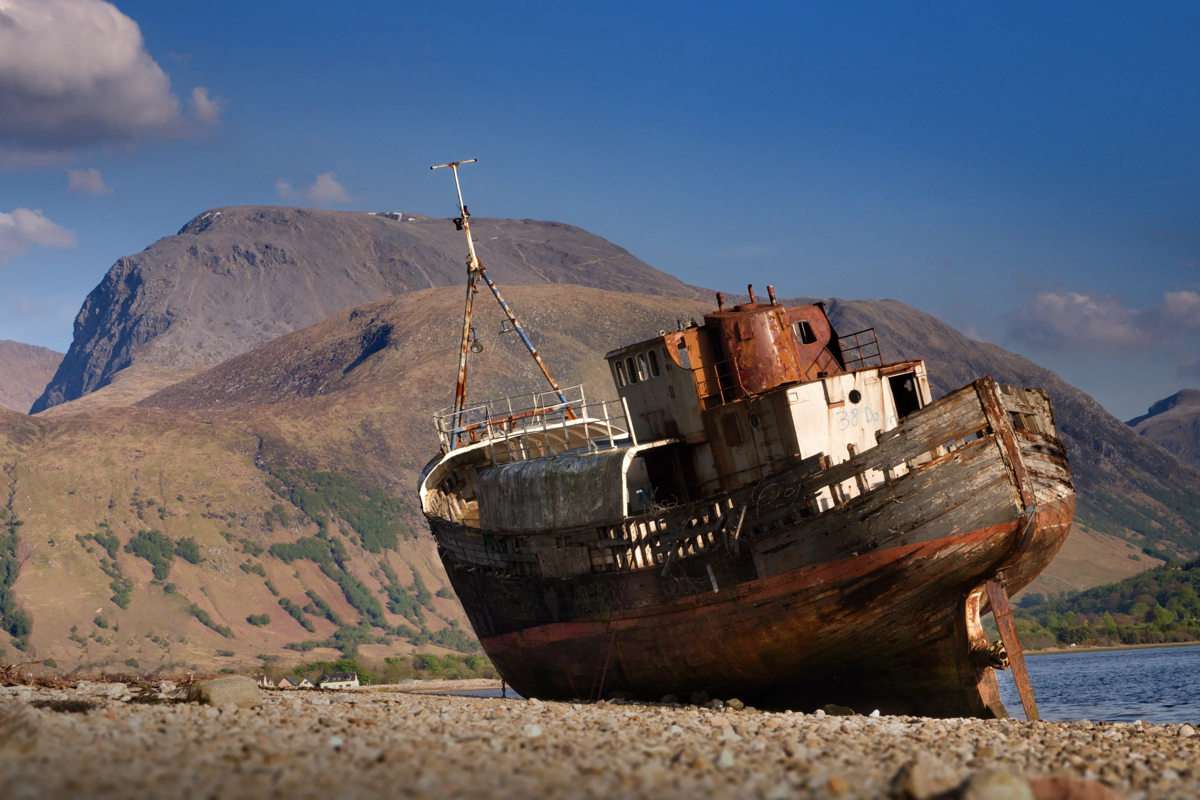 There's a strong chance this image contains the following subjects: sky,  water,  travel,  sea,  scotland,  scottishhighlands,  corpach,  fortwilliam,  bennevis. The photographer has provided the following description: The Corpach shipwreck is actually the rusting remains of a fishing vessel known as 'MV Dayspring'. The 26 metre-long boat was built in 1975. It is found just a couple of miles away from beautiful Fort William. Here, you can see the beast that is Ben Nevis towering over the ship! Photographer_name: Chris Michael. Title: Corpach Shipwreck. The photographer has provided the following description: The Corpach shipwreck is actually the rusting remains of a fishing vessel known as 'MV Dayspring'. The 26 metre-long boat was built in 1975. It is found just a couple of miles away from beautiful Fort William. Here, you can see the beast that is Ben Nevis towering over the ship! Make: fujifilm. Model: x-T5. Technical: 55-200mm. Published: 2025-09-08 16:47:33