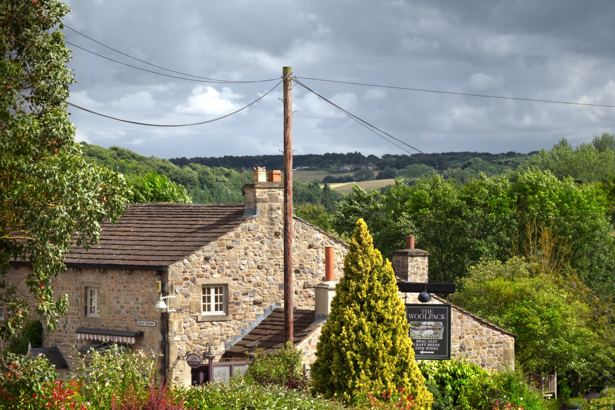 There's a strong chance this image contains the following subjects: tree,  house,  architecture,  travel,  yorkshire,  pub. The photographer has provided the following description: Looks like a beautiful country pub, when in fact this is the Woolpack pub, not a real one, but the one used in the ITV soap Emmerdale. Top Secret: the bricks on the chimney are actually painted on...they're not real bricks. This is on the working set of Emmerdale near Leeds on the Harewood Estate. Photographer_name: Chris Michael. Title: Emmerdale. The photographer has provided the following description: Looks like a beautiful country pub, when in fact this is the Woolpack pub, not a real one, but the one used in the ITV soap Emmerdale. Top Secret: the bricks on the chimney are actually painted on...they're not real bricks. This is on the working set of Emmerdale near Leeds on the Harewood Estate. Make: fujifilm. Model: X-t5. Technical: 16-80mm.. Published: 2025-09-07 23:34:05