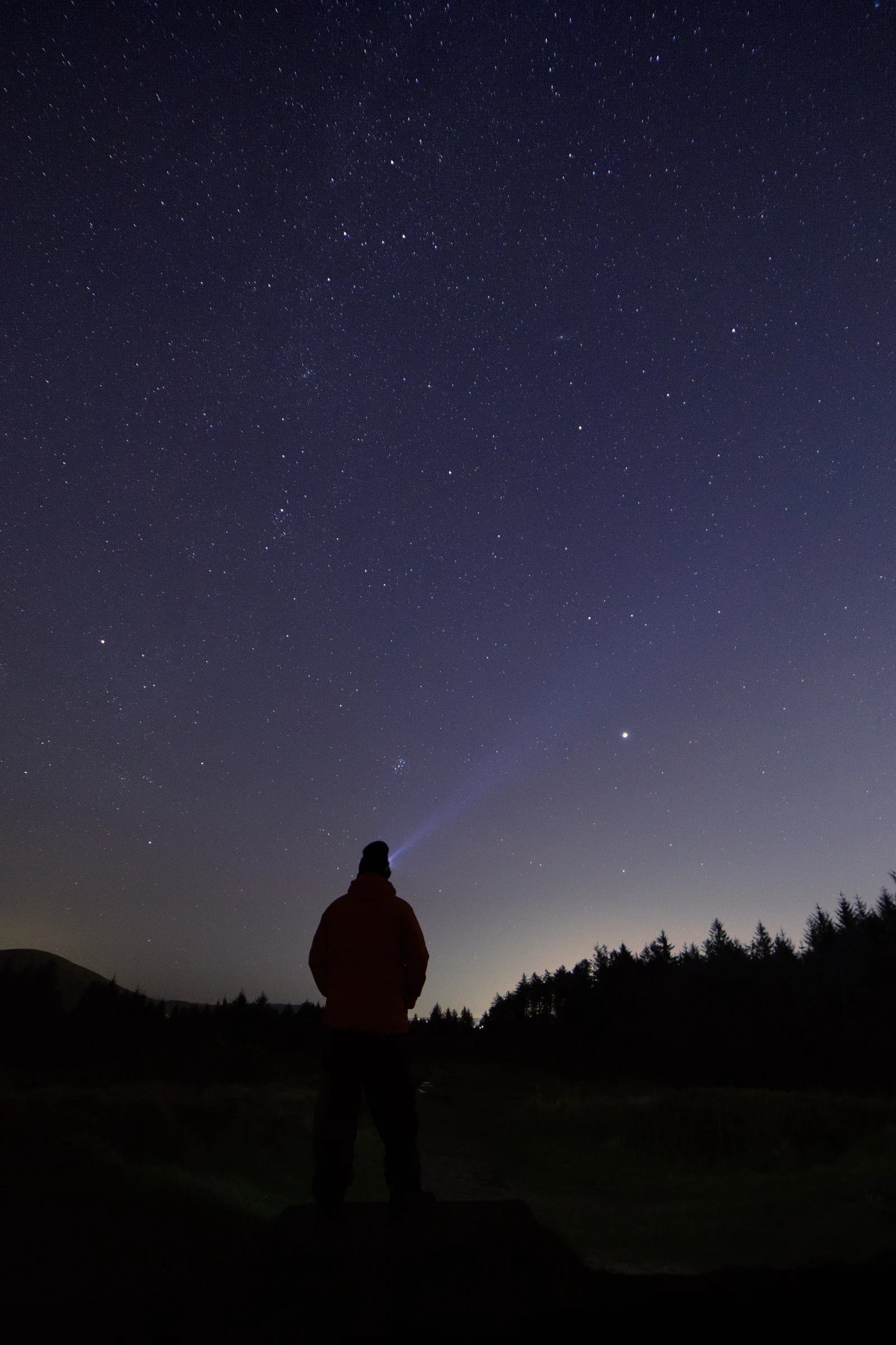 There's a strong chance this image contains the following subjects: sky,  light,  landscape,  people,  preston,  beaconfell,  moon,  astronomy,  galaxy,  chrismichael. The photographer has provided the following description: This was my first ever attempt at taking an astro shot 2023! Taken at the summit of Beacon Fell Country Park north of Preston. This is me, with a winter hat on because it was freezing, and a head torch shining into the sky. I had to stand super still for this photo which was on a 10 second timer, and then stood still for another 20 seconds. Photographer_name: Chris Michael. Title: Star Gazing. The photographer has provided the following description: This was my first ever attempt at taking an astro shot 2023! Taken at the summit of Beacon Fell Country Park north of Preston. This is me, with a winter hat on because it was freezing, and a head torch shining into the sky. I had to stand super still for this photo which was on a 10 second timer, and then stood still for another 20 seconds. Make: canon. Model: EOS R. Technical: Canon RF16mm lens. . Published: 2025-09-07 17:07:56