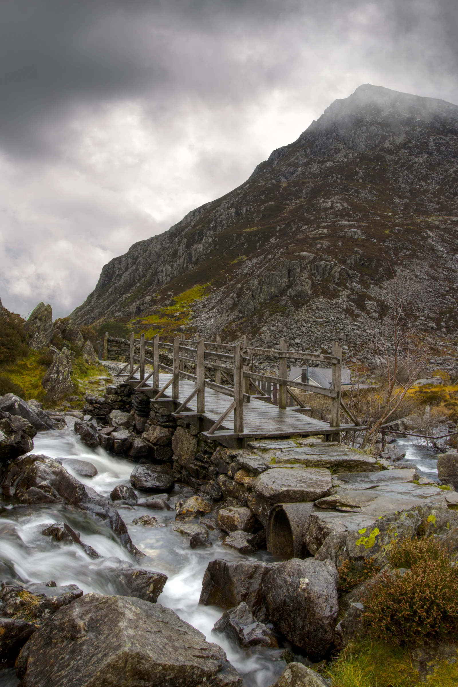 There's a strong chance this image contains the following subjects: water,  landscape,  travel,  nature,  bridge,  wales,  snowdonia,  eryri,  eryrinationalpark,  nationalpark,  snowdon,  penyrolewen. The photographer has provided the following description: Taken at Cwm Idwal Nature Reserve in Snowdonia, Wales. Pen Yr Ole Wen in the background. Photographer_name: Chris Michael. Title: The Bridge. The photographer has provided the following description: Taken at Cwm Idwal Nature Reserve in Snowdonia, Wales. Pen Yr Ole Wen in the background. Make: fujifilm. Model: X-T5. Technical: 16-80mm. Published: 2025-09-09 14:18:17