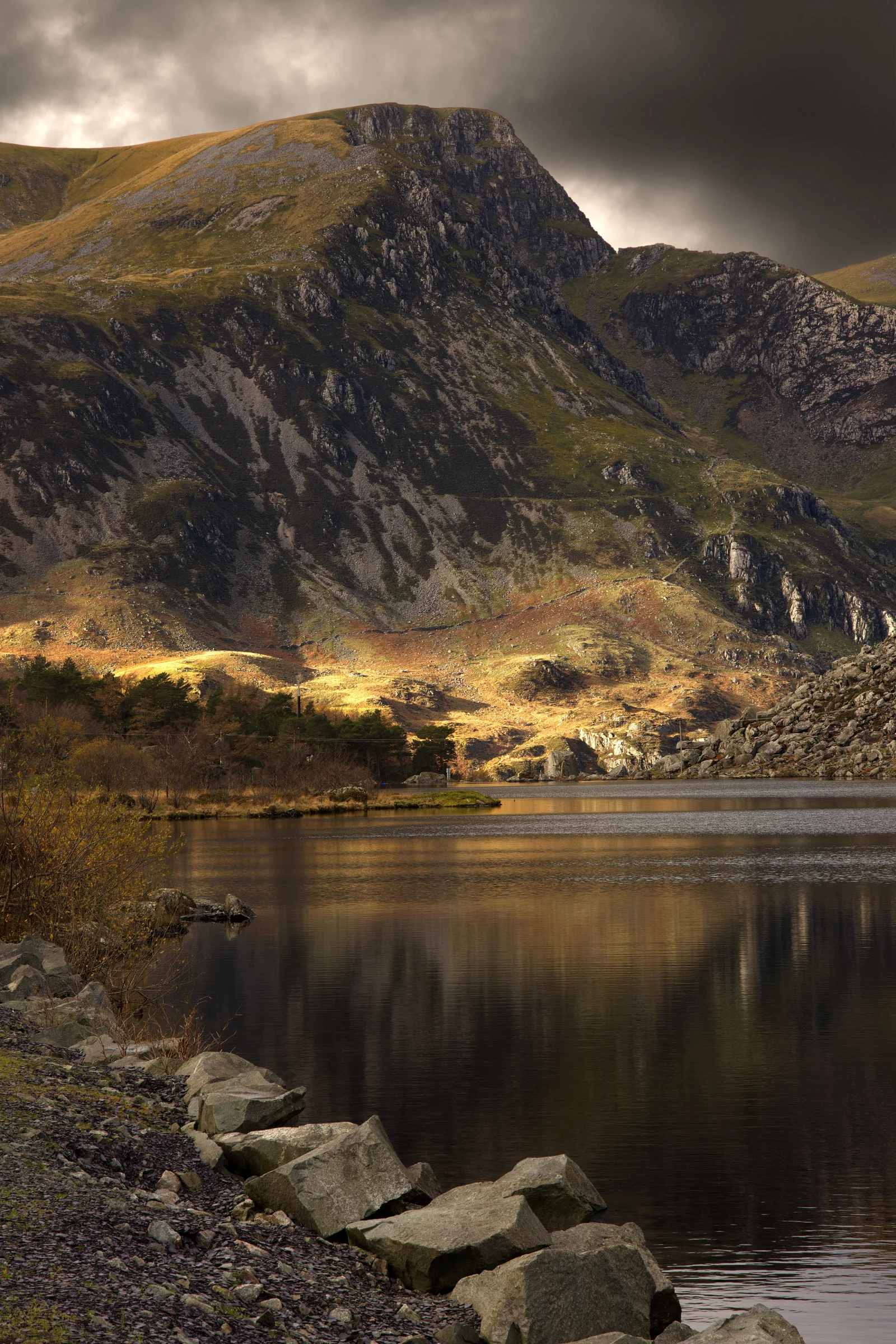 There's a strong chance this image contains the following subjects: light,  landscape,  lake,  nature,  reflection,  wales,  snowdonia,  eryri,  eryrinationalpark,  nationalpark,  snowdon. The photographer has provided the following description: I was lucky to be able to capture this, with the light streaking down the side of a mountain in the distance. Taken from Llyn (lake) Ogwen. Photographer_name: Chris Michael. Title: Snowdonia Light. The photographer has provided the following description: I was lucky to be able to capture this, with the light streaking down the side of a mountain in the distance. Taken from Llyn (lake) Ogwen. Make: fujifilm. Model: X-T5. Technical: 16-80mm. Published: 2025-09-09 16:23:04