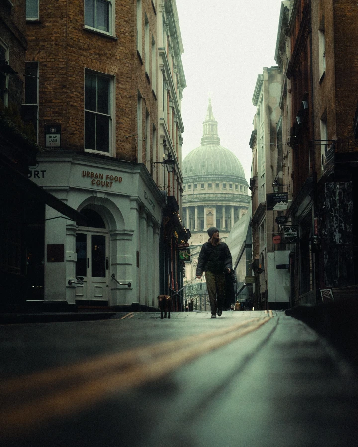 There's a strong chance this image contains the following subjects: architecture,  street,  travel,  city,  church. The photographer has provided the following description: A little bit of rain, perfect wet and matted floors for reflections and some insane fog. FOTO has this to say about the photograph: A gentle rain, slick pavements, and a blanket of thick fog set the stage for this atmospheric London scene. Captured from a low angle, the photograph reveals glistening reflections on the matted ground as a solitary figure walks her dog through the mist, creating a quiet, cinematic moment that feels both intimate and surreal. Source: https://www.instagram.com/keepovisuals/ Photographer_name: Keepo. Title: Foggy days in the city. The photographer has provided the following description: A little bit of rain, perfect wet and matted floors for reflections and some insane fog. FOTO has this to say about the photograph: A gentle rain, slick pavements, and a blanket of thick fog set the stage for this atmospheric London scene. Captured from a low angle, the photograph reveals glistening reflections on the matted ground as a solitary figure walks her dog through the mist, creating a quiet, cinematic moment that feels both intimate and surreal. Published: 2025-06-16 15:00:36