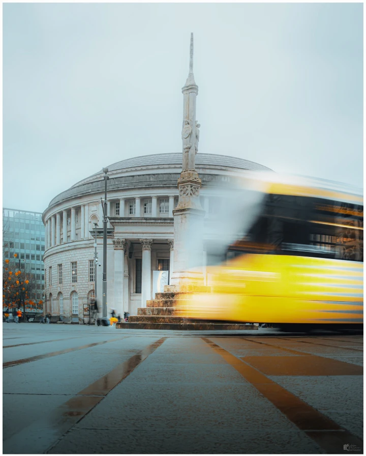 There's a strong chance this image contains the following subjects: architecture,  street,  travel,  city,  urban,  train,  locomotive. The photographer has provided the following description: Swapping the streets of London for the streets of Manchester, where movement, light, and atmosphere tell a different kind of story. FOTO has this to say about the photograph: Motion and mood converge in this dynamic photograph of Manchester Central Library, where a passing tram blurs through the frame and rain-slicked streets reflect the city’s glow. The depth and texture create a cinematic quality that brings the scene vividly to life. Source: https://www.instagram.com/ap__visuals/ Photographer_name: Adam Palmer. The photographer has provided the following description: Swapping the streets of London for the streets of Manchester, where movement, light, and atmosphere tell a different kind of story. FOTO has this to say about the photograph: Motion and mood converge in this dynamic photograph of Manchester Central Library, where a passing tram blurs through the frame and rain-slicked streets reflect the city’s glow. The depth and texture create a cinematic quality that brings the scene vividly to life. Published: 2025-06-13 15:37:48